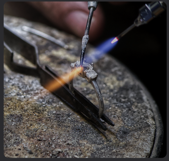 Lötprozess mit Flamme auf einem Schmuckstück in einer Werkstatt.